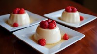 Creamy vanilla panna cotta desserts topped with fresh raspberries served on white square plates, elegant restaurant presentation for fine dining menu.