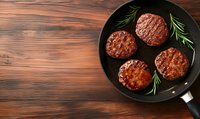 Grilled beef patties with fresh rosemary sprigs in black cast iron pan on rustic wooden background, top view. Food photography for restaurant menu.
