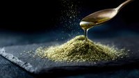 Golden honey dripping from spoon onto pile of green matcha tea powder, creating artistic splash effect on dark stone surface. Food photography concept.