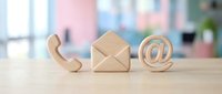 Wooden contact symbols on desk showing phone, email and at sign for business communication and customer service concepts.
