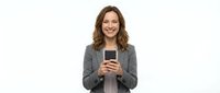 Smiling woman with long brown wavy hair, Caucasian ethnicity, wearing gray blazer, holding smartphone, isolated on white background for business and technology use.
