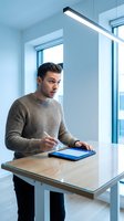 Young Caucasian businessman in beige sweater using digital tablet with stylus pen at modern office desk near window for creative work and productivity.