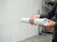 Architect or construction worker holding rolled white blueprint or architectural plan on indoor building site with concrete wall background.