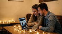 Young couple enjoying video call on laptop in cozy candlelit room, sharing intimate moment together during evening communication with friends or family.