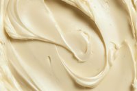 Creamy vanilla frosting texture with smooth swirls and waves creating an abstract pattern background, close up macro shot showing rich buttery consistency.