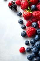 Fresh mixed berries scattered on white background with dramatic lighting. Strawberries, blueberries, raspberries and blackberry create appetizing composition.