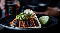 Gourmet beef tacos with guacamole and fresh vegetables served on dark plate in upscale restaurant setting for culinary marketing and food service promotion.