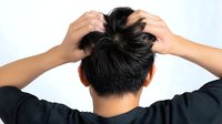 Young Asian man scratching head with both hands showing scalp irritation and dandruff problem against white background, rear view perspective.