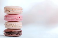 Stack of colorful French macarons in pastel pink and beige tones on white background, featuring delicate meringue cookies with creamy filling.