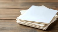 Stack of blank white paper sheets scattered on wooden table surface with natural lighting and shallow depth of field, suitable for business and office concepts.