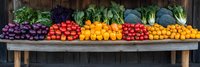Fresh colorful vegetables and fruits arranged in rainbow order on rustic wooden shelf including beets, tomatoes, peppers, citrus, and leafy greens against dark wood background.