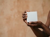 Hands of person with dark skin tone holding blank white card against neutral beige background for branding, marketing, or business messaging.