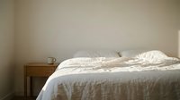 Unmade bed with white linens and wooden nightstand in minimalist bedroom interior, suitable for home decor and lifestyle content.