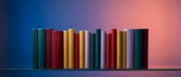 Row of colorful books standing on shelf against gradient background for education, library, reading and literature concepts.