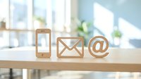 Wooden communication icons on desk featuring smartphone, envelope and email symbol in bright modern office interior for digital marketing concepts.