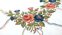 Embroidered floral bouquet with coral and blue roses on white fabric, traditional needlework craft with colorful threads for handmade textile projects.