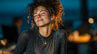 Young mixed-race woman with curly hair smiling peacefully with eyes closed in warm evening light. Relaxation, mindfulness and positive emotions concept.