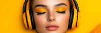 Young woman with closed eyes wearing black and yellow headphones against bright yellow background. Vibrant orange eyeshadow makeup creates striking contrast.