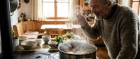 Senior Caucasian man cooking healthy meal in rustic kitchen, steam rising from pot, natural lighting, homemade food preparation, domestic lifestyle concept.