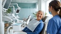 Senior woman patient smiling during dental consultation with female dentist in modern clinic office for oral health checkup and treatment.