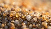 Macro shot of raw amber and quartz crystals scattered on sandy surface, showcasing natural mineral textures and warm golden tones for geology and nature backgrounds.