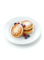 Fluffy pancakes dusted with powdered sugar, topped with fresh raspberries and blueberries on white plate. Breakfast and brunch food photography.