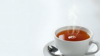 Hot steaming tea in white ceramic cup and saucer with spoon on clean background for beverage and relaxation concepts.