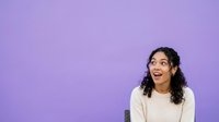 Young woman with long dark curly hair and medium skin tone wearing cream sweater, expressing surprise or excitement against purple background for advertising and marketing campaigns.