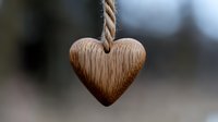 Rustic wooden heart pendant hanging from natural twine rope against blurred background, symbolizing love, craftsmanship and eco-friendly design elements.