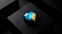 Polished labradorite gemstone with brilliant blue and golden flash on dark textured surface for luxury jewelry and mineral collection displays.
