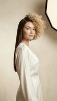 Young mixed-race woman with half straight half curly blonde hair in white robe portrait for beauty salon hair styling transformation concept.