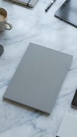 Gray blank notebook on marble desk with coffee cup and office supplies for business planning and creative work.