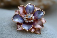 Delicate rose gold flower brooch with purple and pink enamel petals, adorned with sparkling crystals in center, showcased on soft linen fabric background.