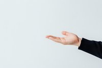 Caucasian female hand in black sleeve making open palm gesture against light background, expressing support, offering or presenting concept for business use.