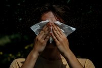 Young woman sneezing into tissue outdoors with pollen particles floating in air during allergy season causing hay fever and respiratory discomfort.