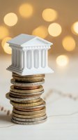 White miniature bank building with classical columns sitting on stack of coins with warm bokeh lights background for financial services concepts.