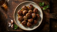 Homemade beef meatballs with herbs served in ceramic bowl on rustic wooden table with garlic and parsley for cooking and dining concepts.