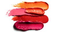 Colorful lipstick smears in vibrant shades of orange, pink, red, and burgundy arranged in horizontal strokes on white background for cosmetic advertising.