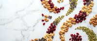 Colorful dried fruits, nuts and seeds arranged in decorative swirls on white marble background. Healthy snacking and organic food ingredients for cooking.
