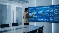 Asian businesswoman presenting data analytics dashboard with charts and graphs on large screen in modern conference room for business meeting.