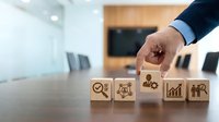 Professional businessman hand arranging wooden blocks with business strategy icons in modern office conference room for corporate planning and development.