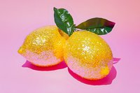 Two lemons with glitter coating and green leaves on pink background, isolated for design use on merchandise and promotional materials.