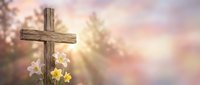 Wooden cross with spring flowers against soft pastel sky background for Easter celebration, religious faith, and spiritual worship concepts.