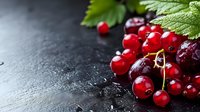 Fresh red currants and sweet cherries with green leaves on dark stone background, macro food photography with copy space for menu design.