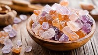 Colorful crystallized sugar candy cubes in wooden bowl on rustic table. Orange and purple rock candy pieces create sweet composition for confectionery designs.