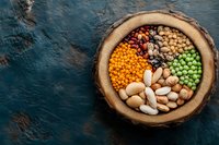 Assortment of colorful legumes and beans in rustic wooden bowl on dark blue textured background, healthy protein sources for vegetarian cuisine.