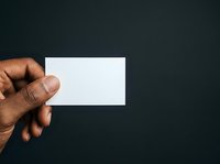 Male hand with dark skin tone holding blank white business card against dark background, suitable for branding and corporate design projects.