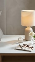 Cozy minimalist bedside table with lamp, open notebook, glasses, water glass and white rose in neutral tones for home decor.