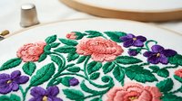Colorful floral embroidery with pink roses and purple violets on white fabric in wooden hoop, traditional needlework craft for home decor projects.