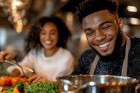 Happy young African American man cooking healthy meal with girlfriend in modern kitchen, smiling while preparing fresh vegetables together at home.